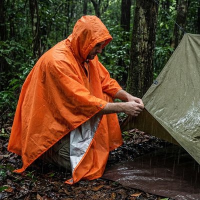 poncho pluie orange homme en camping montant son bivouac